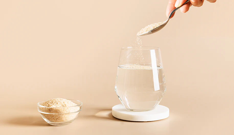 A hand pouring psyllium husk on a glass of water as the person Incorporates Psyllium Husk in her Diet 