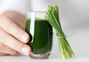 wheatgrass Juice on a glass held by a hand beside a wheatgrass leaves