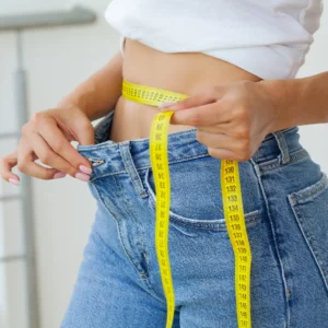a woman showing how she lost weight by pulling her pants and wrapping her waist with a measuring tape