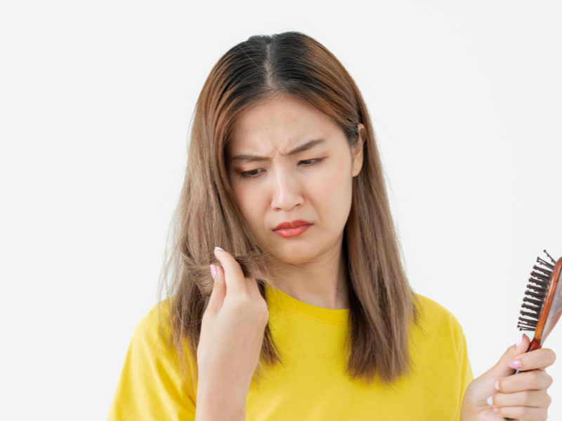Woman in yellow shirt looking at damaged split hair ends