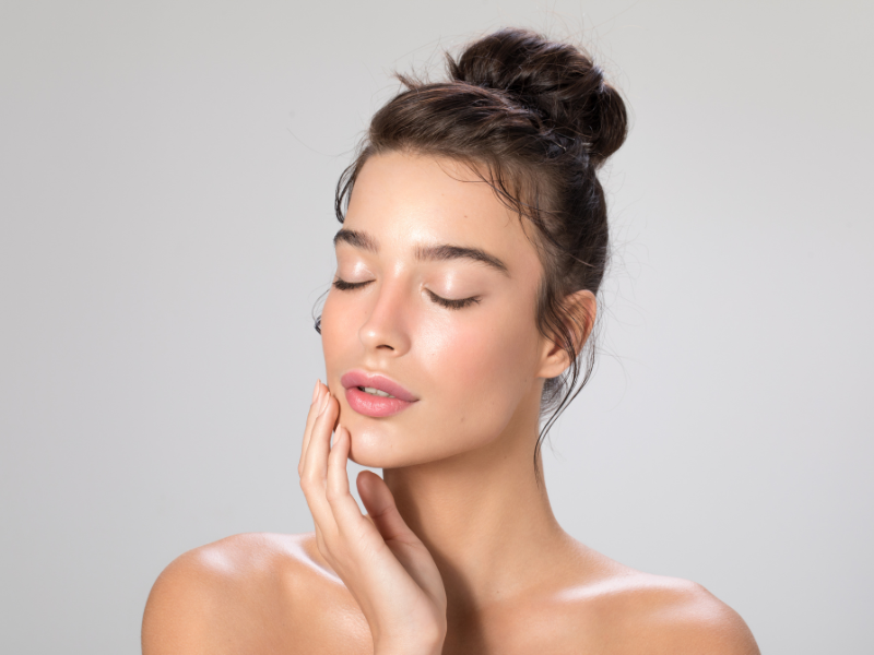 Young woman touching face with glowing, smooth, and healthy skin