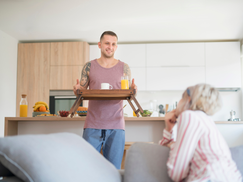 Man carrying breakfast tray to woman sitting on couch smiling