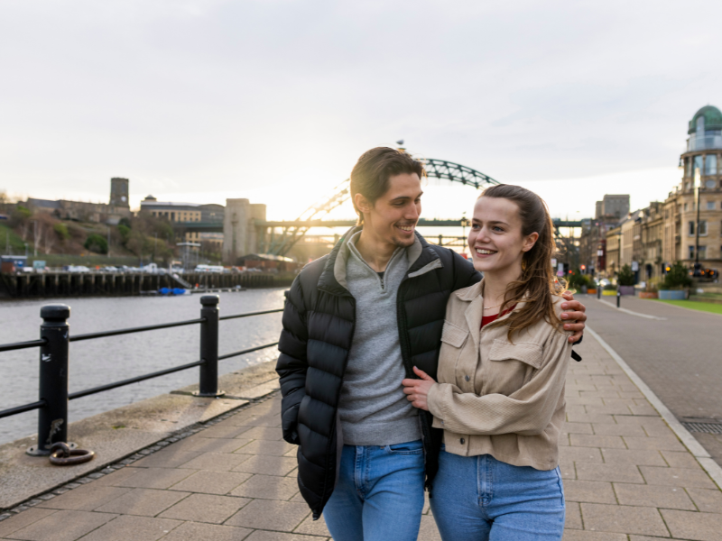 Couple walking by river, smiling, enjoying a peaceful evening together