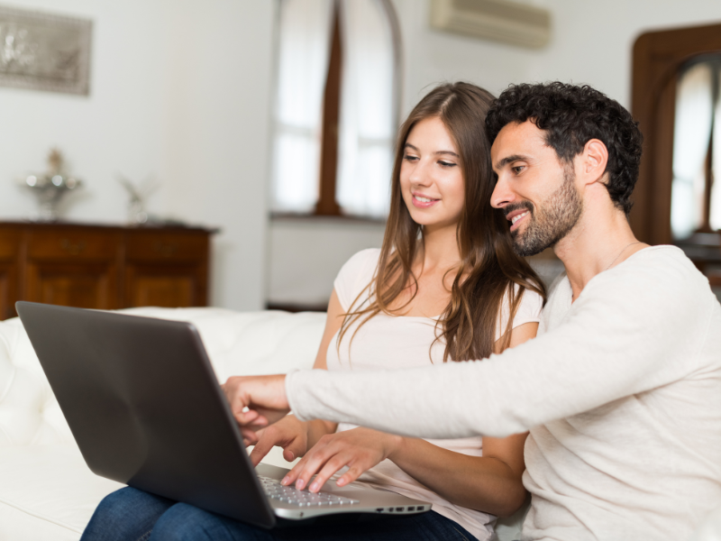 A happy couple sitting together, looking at a laptop screen