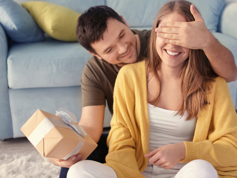 Man covering woman’s eyes while giving her a wrapped present