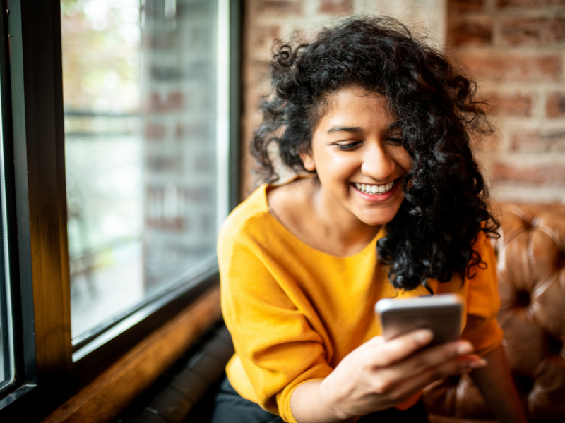 Curly-haired woman laughs while reading a message on phone