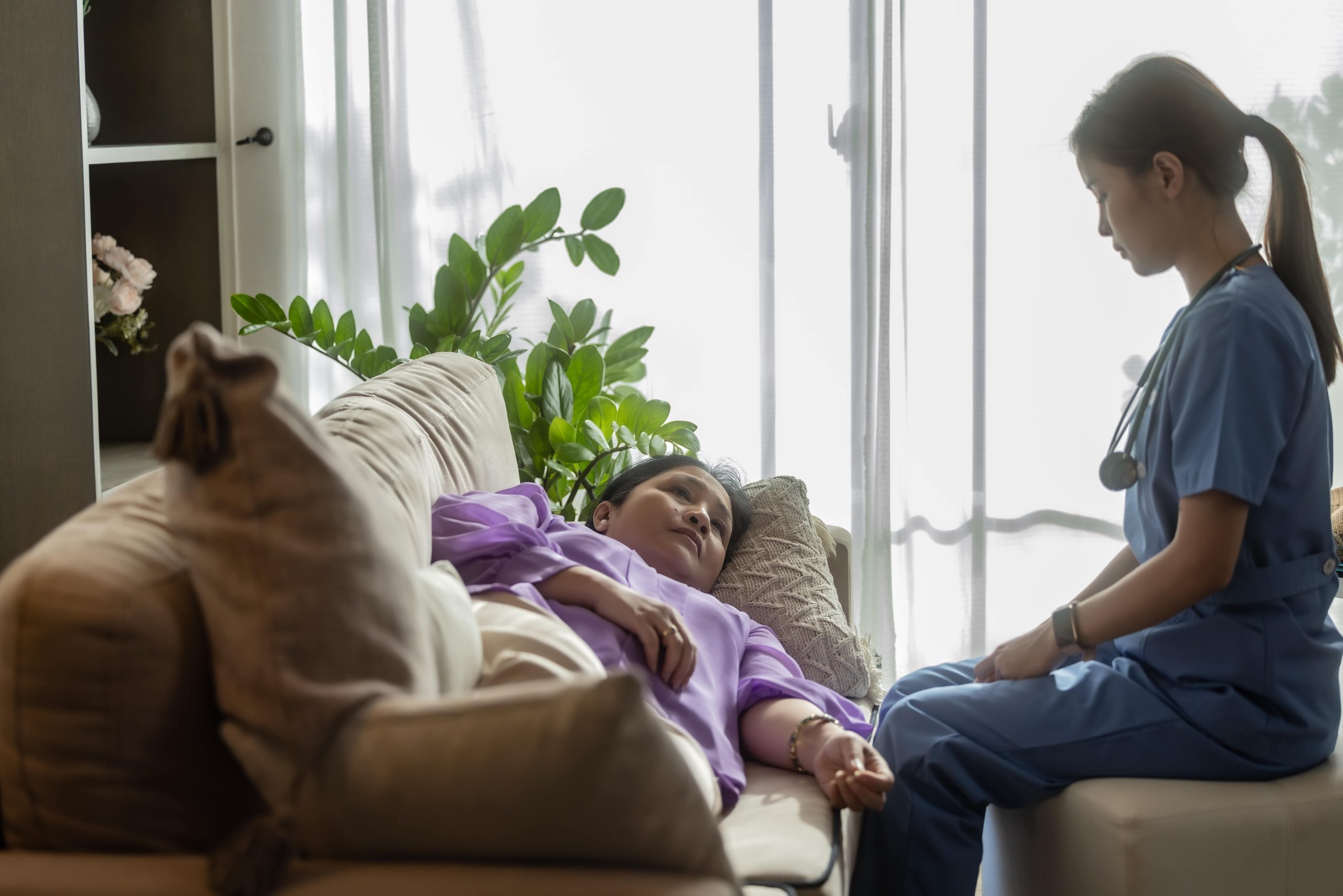 woman recovering on the couch with a healthcare provider looking after her
