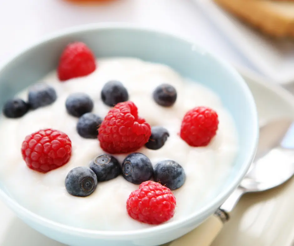 A bowl of creamy yogurt topped with fresh raspberries and blueberries, perfect for a healthy snack