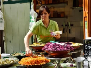 A food vendor serving freshly prepared salad dishes with colorful shredded vegetables at an outdoor market.