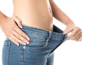 A woman pulling the waistband of her loose blue jeans