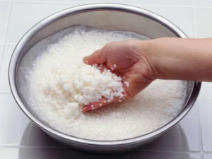 A hand washing white rice grains in a stainless bowl