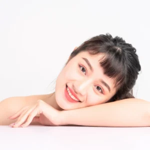 a beauitful asian woman who is happily looking at the camera while head resting on her arm