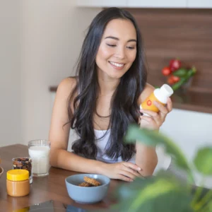 an asian woman looking at a bottle of glutathione after having breakfast